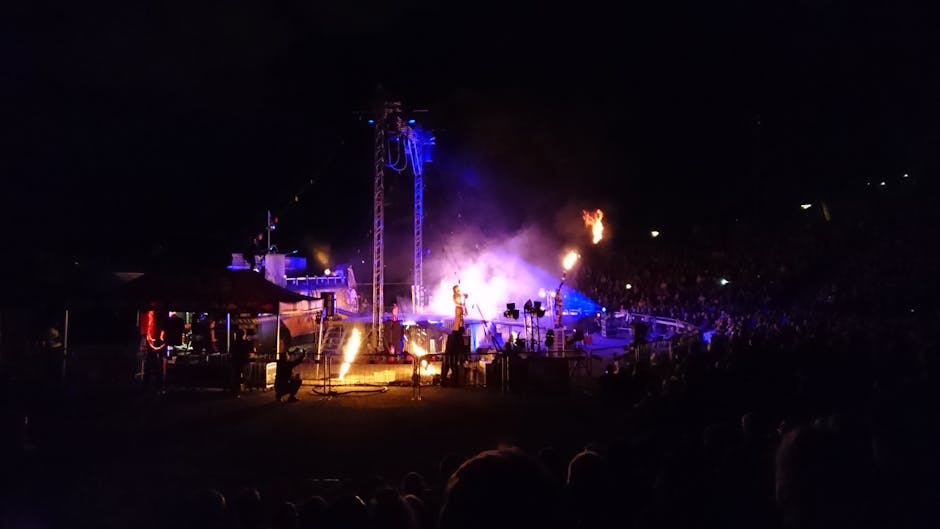 A vibrant live performance showcasing pyrotechnics, lights, and a large crowd at night